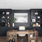 Chic black and brown home office boasts a brown wooden desk matched with a white and brown desk chair placed in front of black built-in cabinets fixed under black shelves flanking a black and white photograph.
